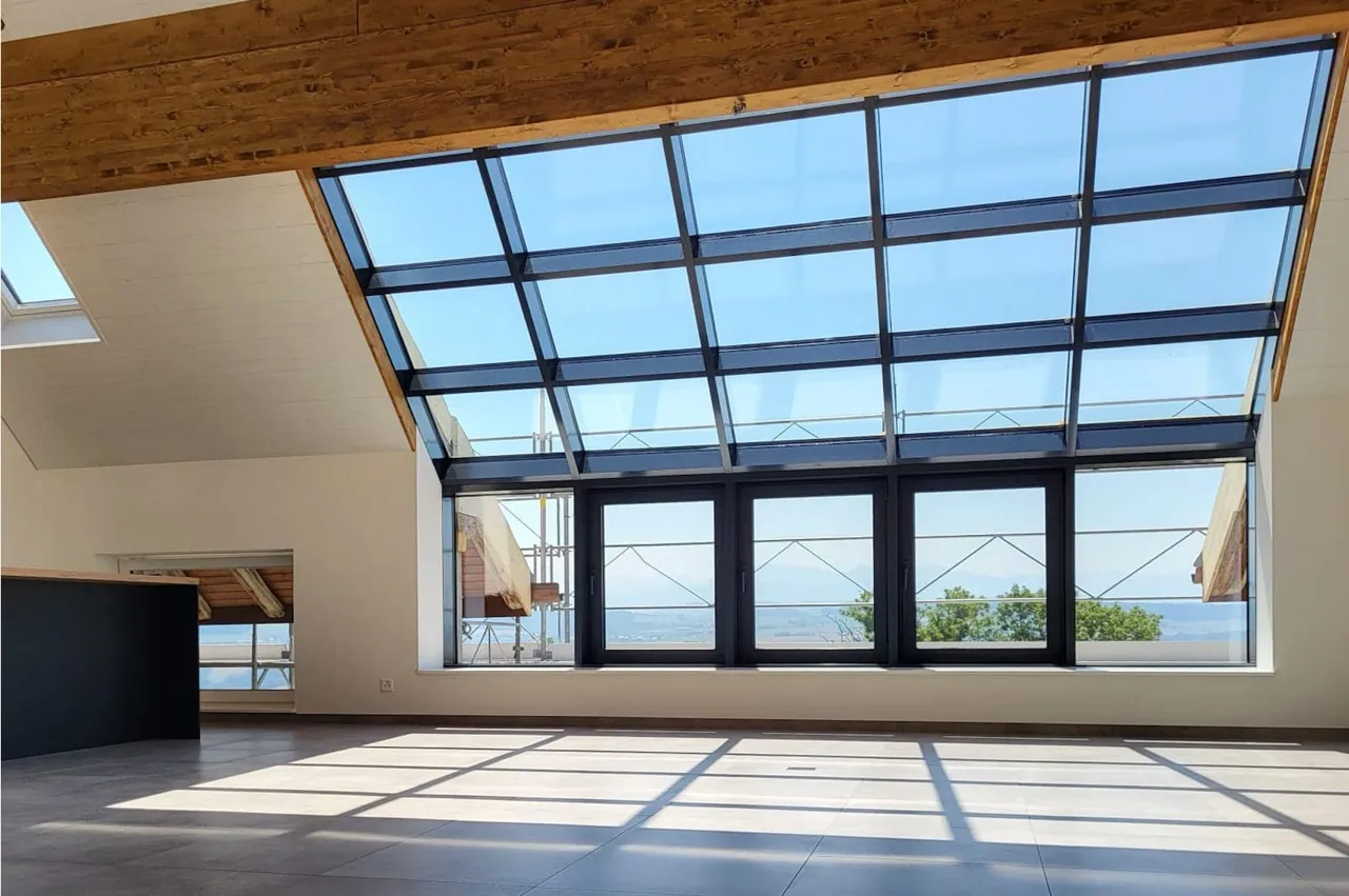 Interior under timber beams with a large sloped glazed wall and integrated door