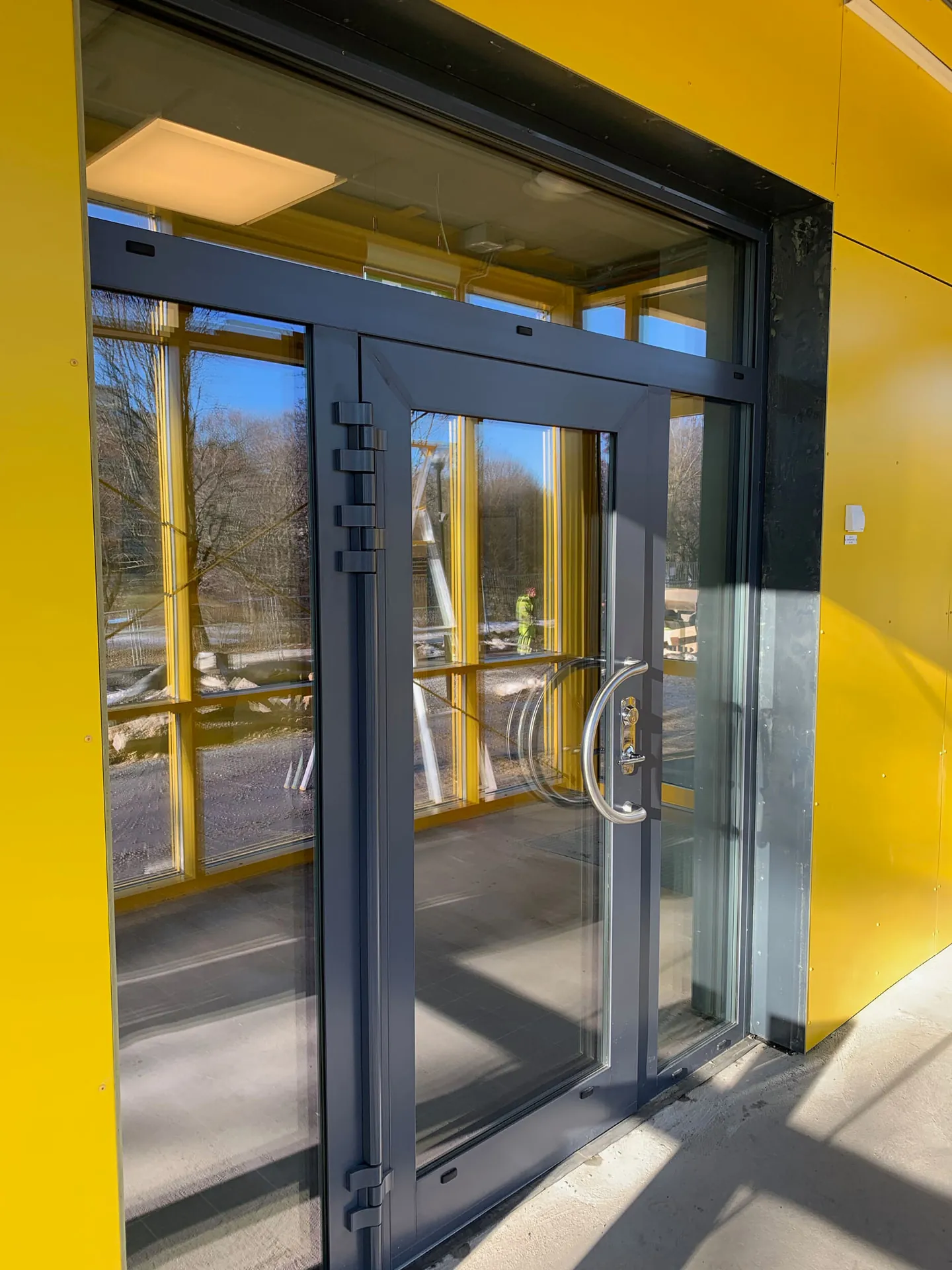 Yellow-clad building elevation with a dark-framed glazed entrance door set
