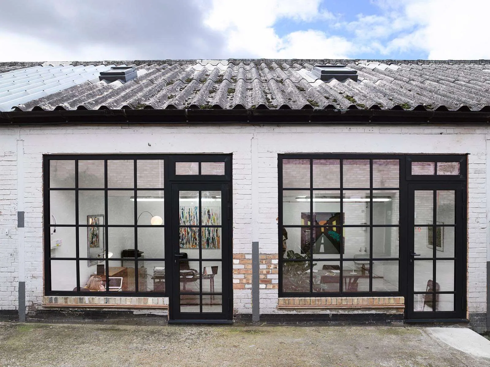 White brick frontage with two black-framed glazed door and window sets to separate studio units